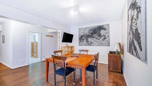 Un comedor con una mesa y sillas de madera, un televisor de pantalla plana montado en la pared y obras de arte en las paredes.
