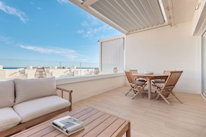 A balcony with a sofa, a table, and chairs, overlooking a cityscape and the sea. - Playa Paraiso Beachfront Apartment (La Vila Joiosa)