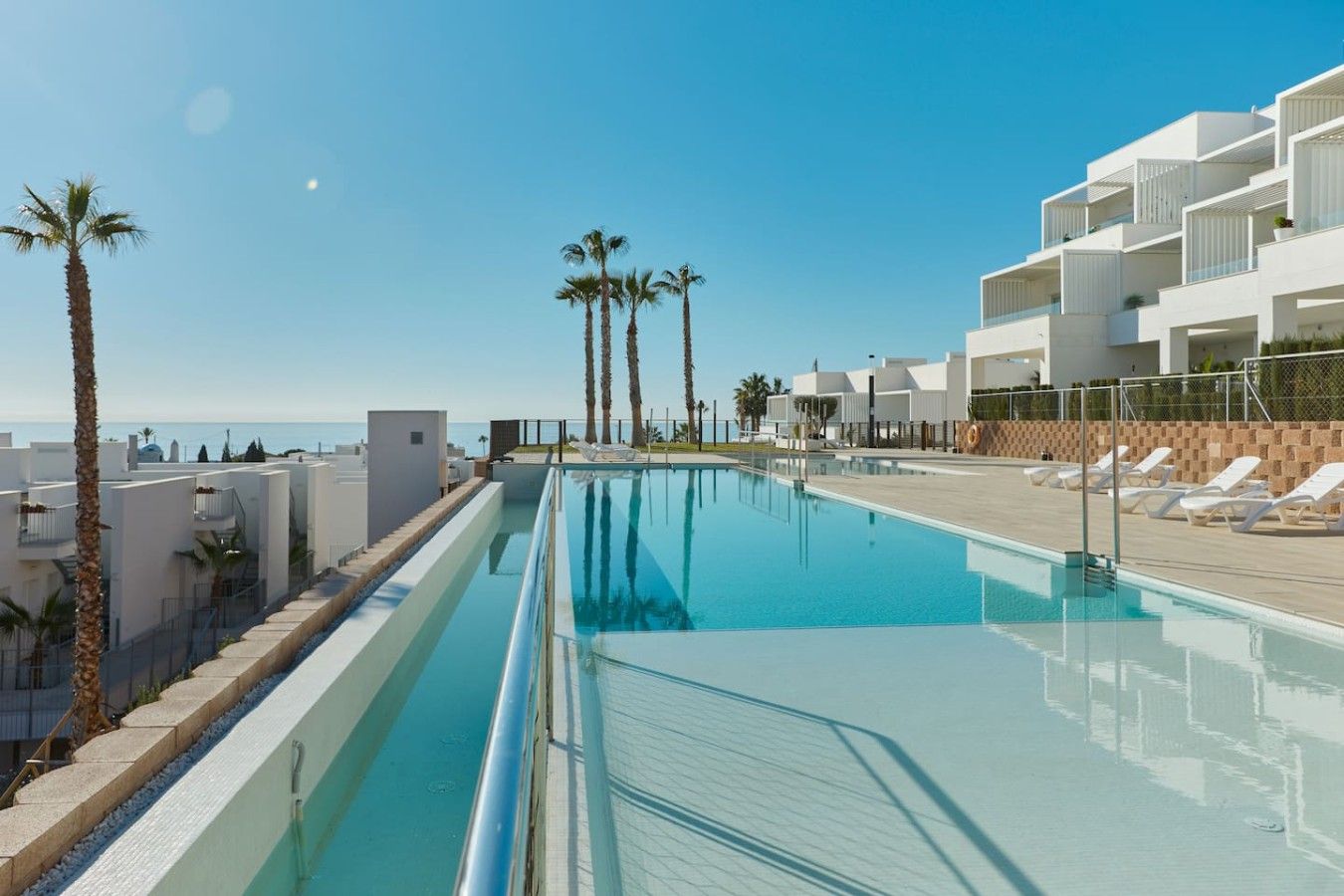 A swimming pool with lounge chairs and palm trees, surrounded by modern buildings.