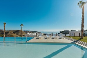 A swimming pool with lounge chairs and palm trees, overlooking a coastal landscape. - Playa Paraiso Beachfront Apartment (La Vila Joiosa)