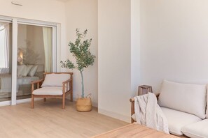 A living room with a wooden chair, a sofa, a small table, and a potted plant. - Playa Paraiso Beachfront Apartment (La Vila Joiosa)