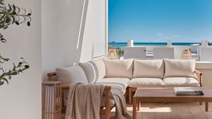 A modern living room with a sofa and coffee table, a wicker chair, and a view of the sea. - Playa Paraiso Beachfront Apartment (La Vila Joiosa)