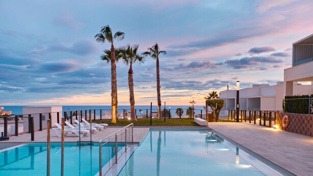 A swimming pool with lounge chairs and palm trees, overlooking a body of water. - Playa Paraiso Beachfront Apartment (La Vila Joiosa)