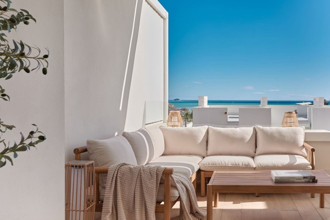 A balcony with a sofa and a table, overlooking a clear blue sky and a distant coastline.