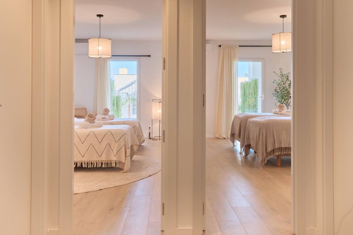 A hotel room with two beds, a large window, and a view of greenery outside.