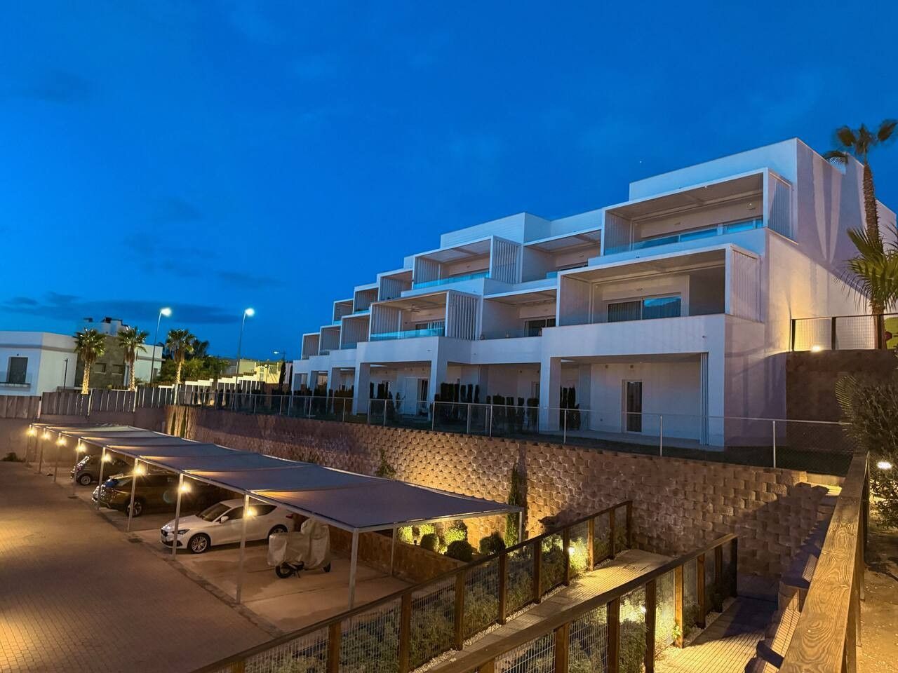A modern hotel with multiple balconies, a covered parking area, and a stone retaining wall.