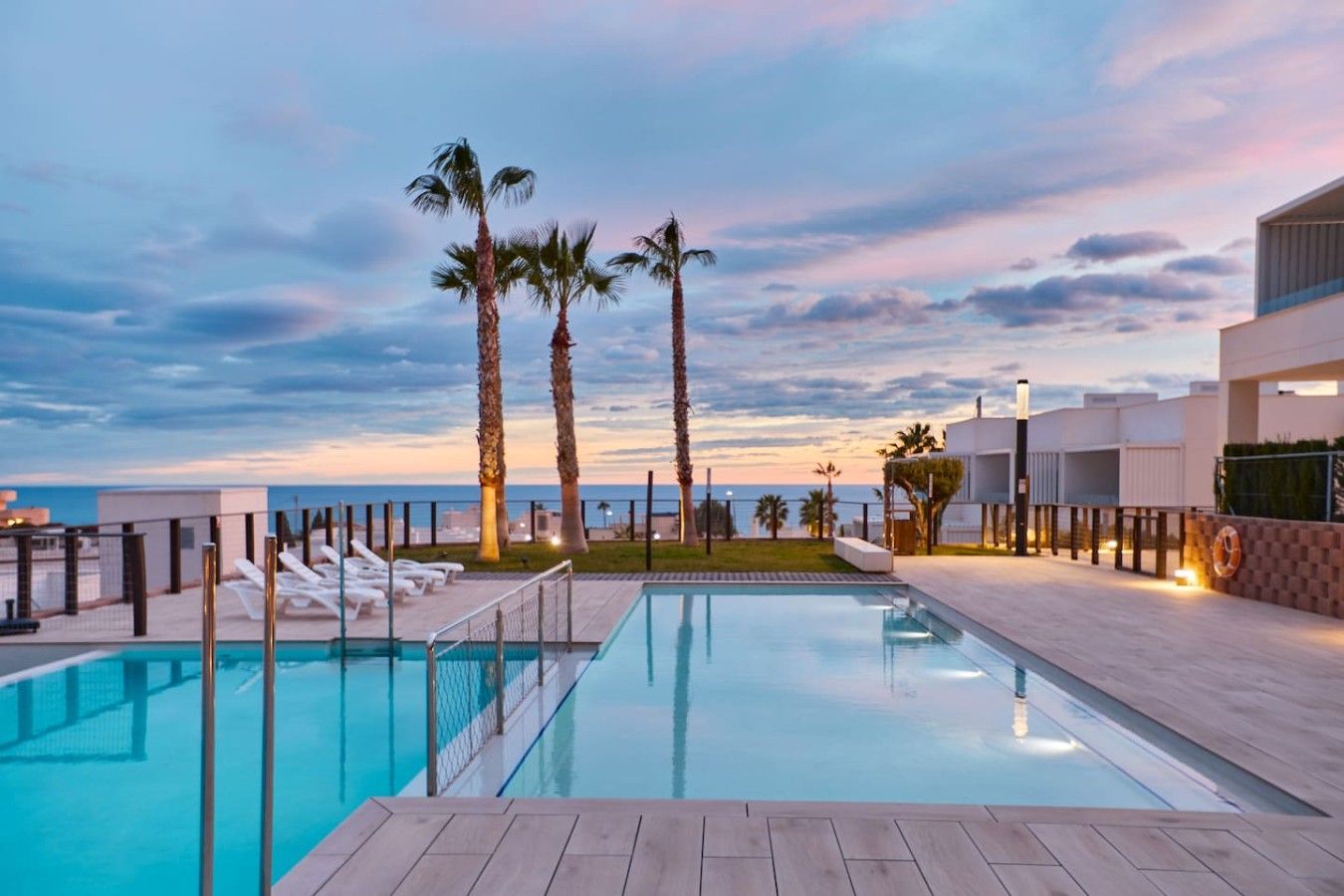 A swimming pool with a view of the sea, surrounded by palm trees and modern architecture.