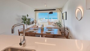 A modern kitchen with a stainless steel sink, wooden dining table set for four, and a view of the balcony with a table and chairs. - Playa Paraiso Beachfront Apartment (La Vila Joiosa)