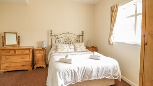 Quarto com cama, mesas de cabeceira em madeira, cômoda e janela com cortinas.