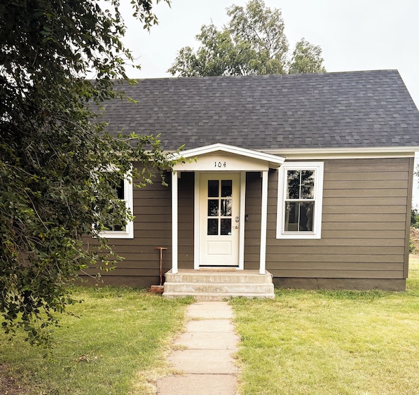 A single-story house with a dark brown siding, a white front door, and the number 104 on the door.