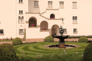 A building with a fountain, manicured garden, and arched windows.