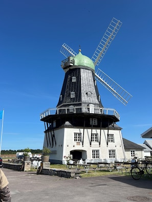 A windmill with a green top and white base, surrounded by outdoor seating and bicycles.