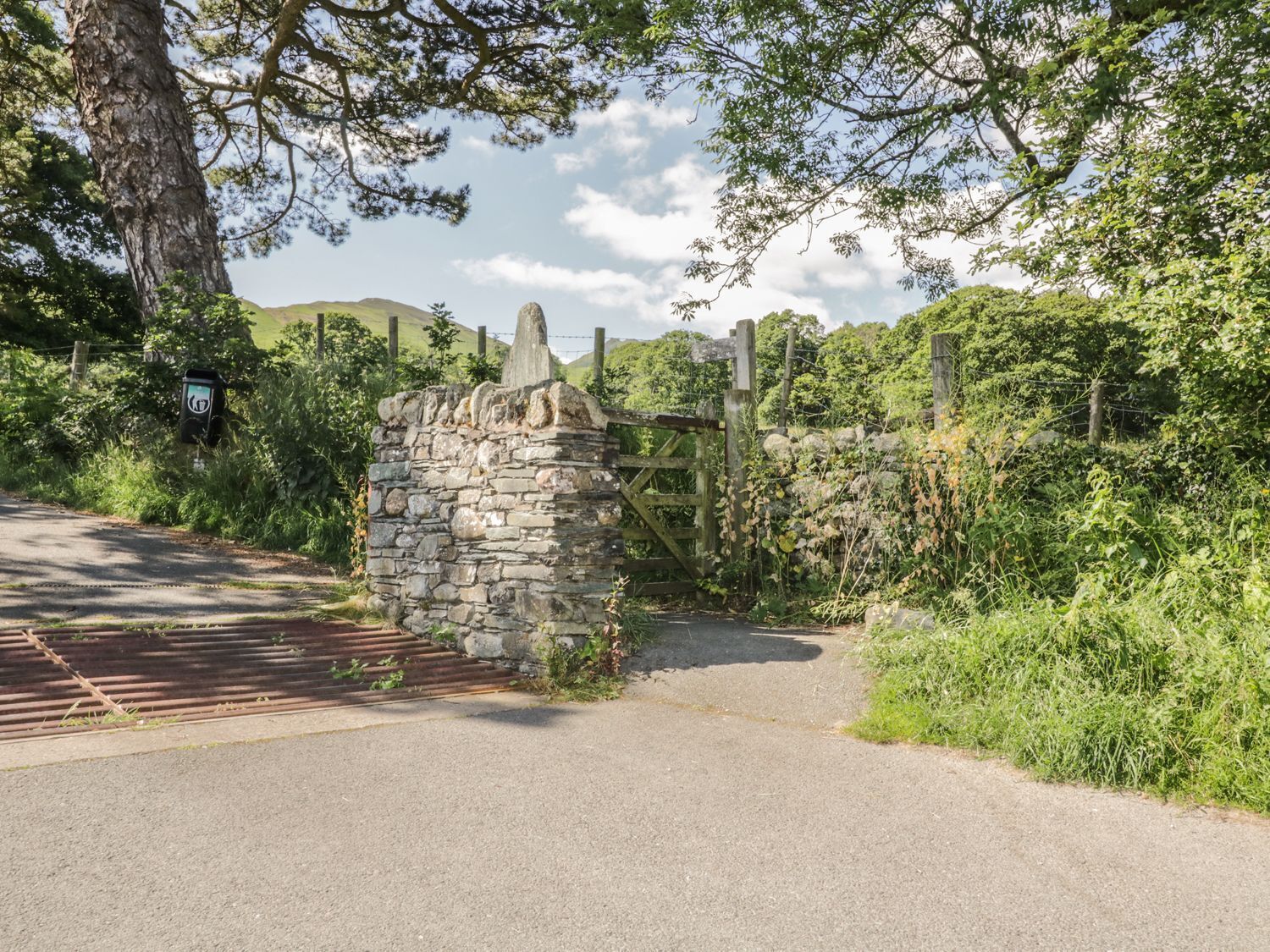 A stone gate leading to a rural road surrounded by greenery and hills.