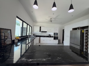 A modern kitchen with a black marble countertop, white cabinets, a built-in oven, and a refrigerator. - Villa CasaYoung "Perfect Family Vacations" Cenotes and Fun Just Minutes Away! (Puerto Morelos)