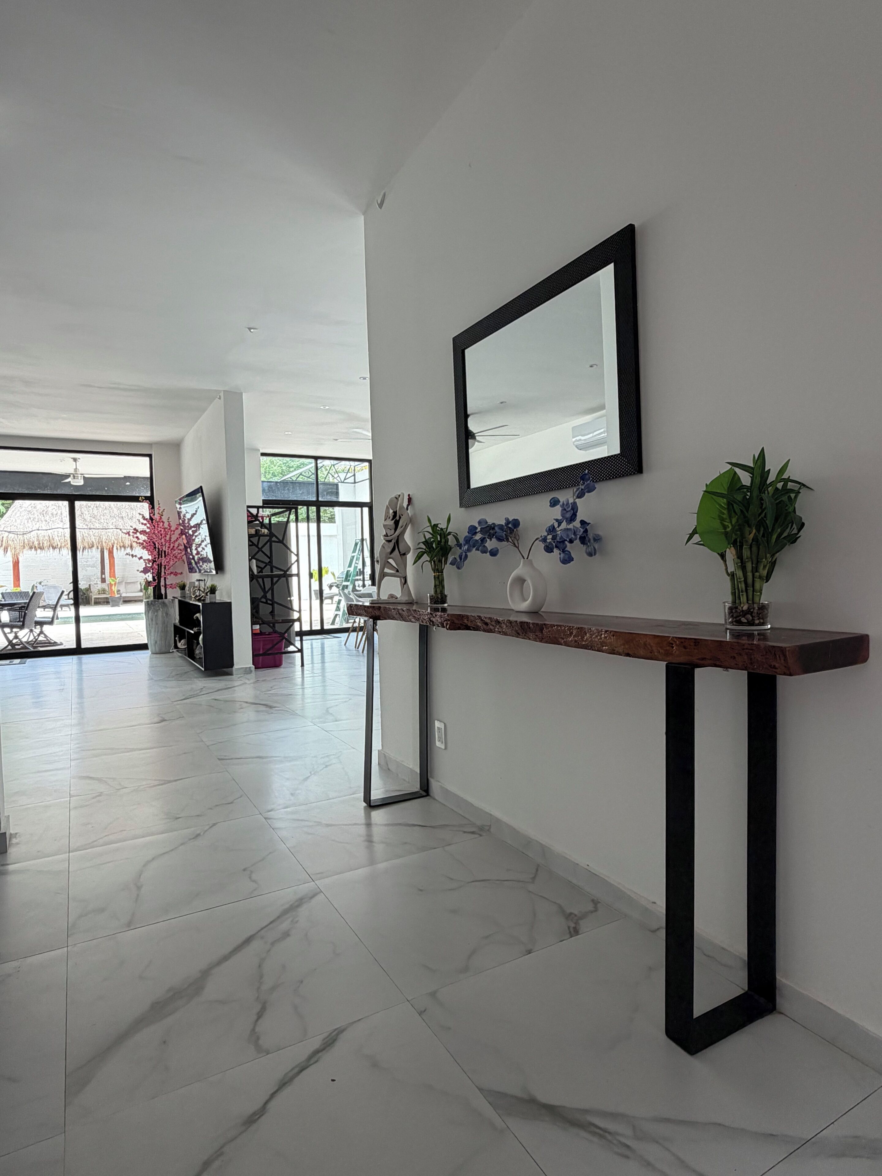 A modern interior with a marble floor, a wooden console table with a mirror, and potted plants.