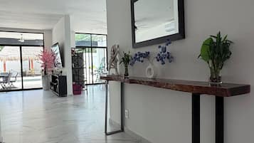 A modern interior with a marble floor, a wooden console table with a mirror, and potted plants.