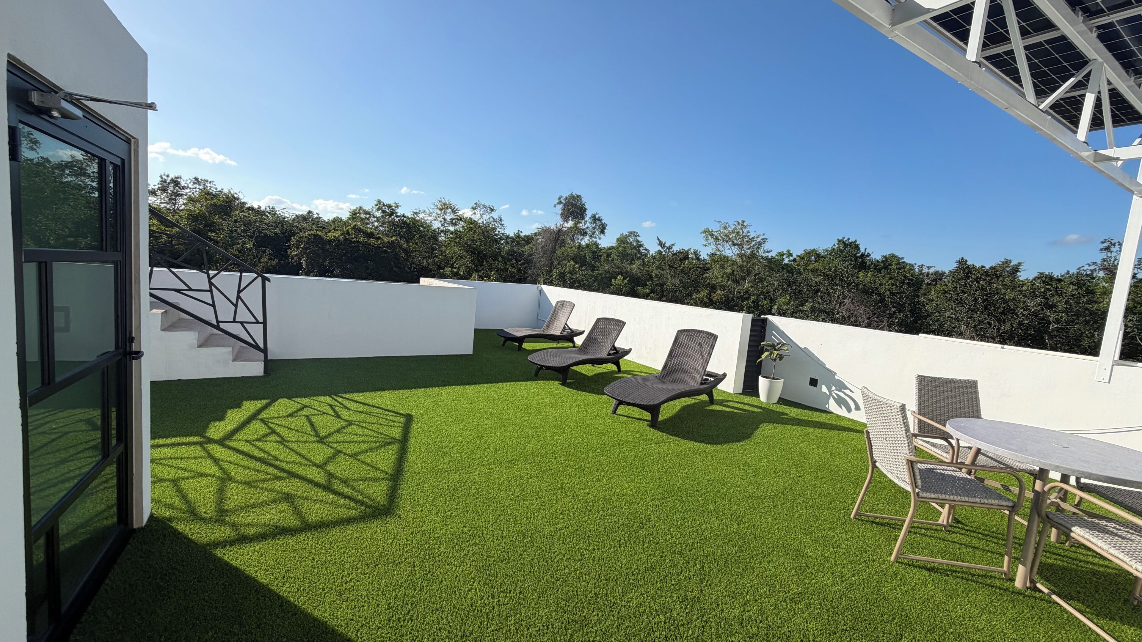 A rooftop with artificial grass, a table, and lounge chairs.