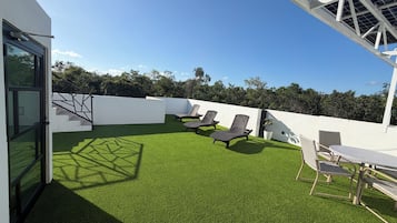 A rooftop with artificial grass, a table, and lounge chairs.