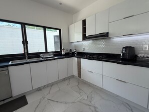 A modern kitchen with white cabinets, a black countertop, a gas stove, and a coffee maker.