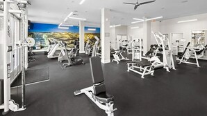Ein Fitnessstudio mit verschiedenen Trainingsgeräten, einer großen Wandmalerei und einem Deckenventilator.