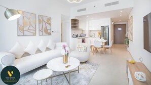 A modern living room with a white sofa, a coffee table, and a dining area with a wooden table and chairs. - Vogue | Downtown with Direct Access to Dubai Mall (Dubai)