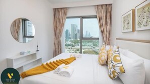 A hotel room with a bed, a round mirror, a window with curtains, and artwork on the wall. - Vogue | Downtown with Direct Access to Dubai Mall (Dubai)