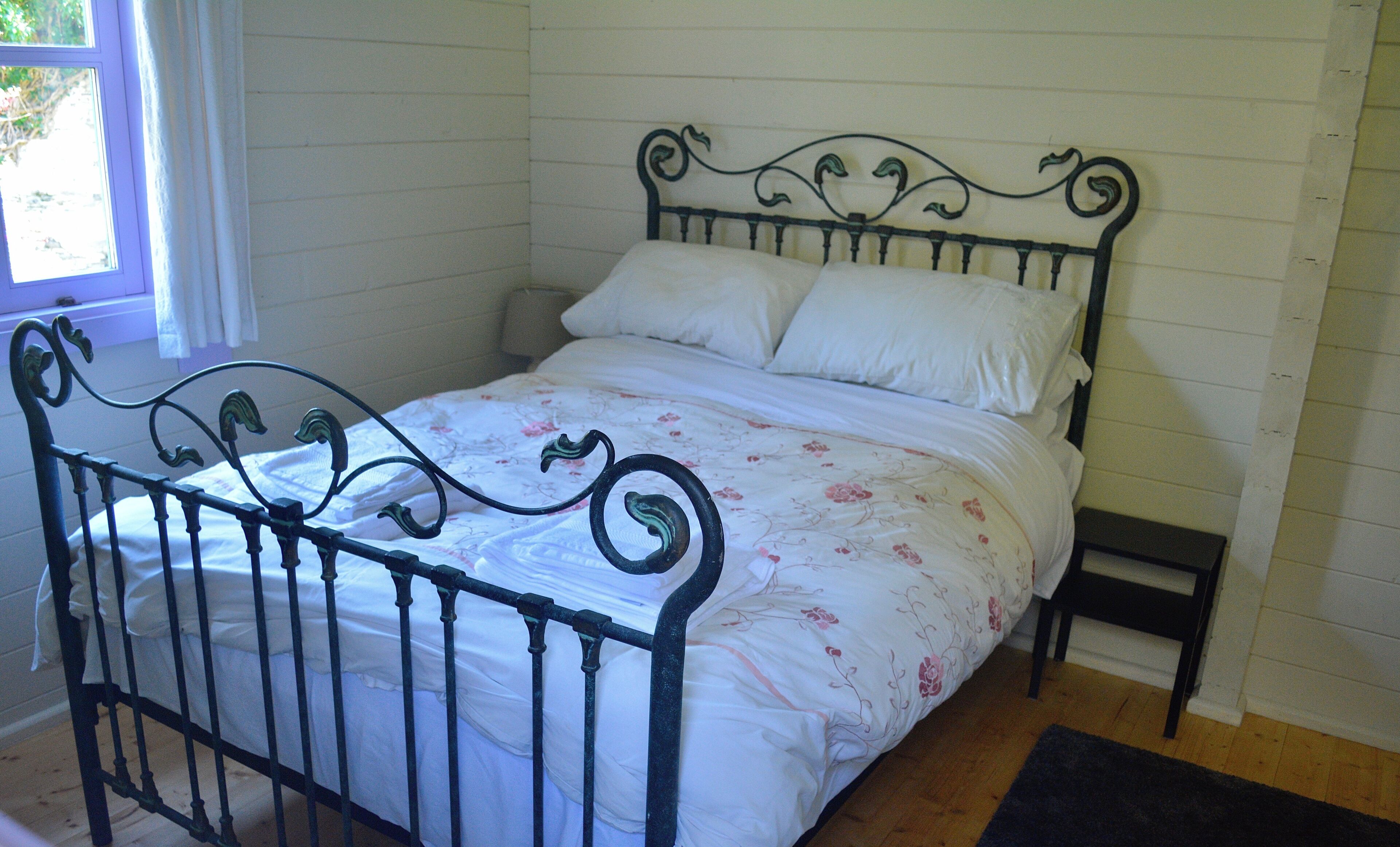 A bed with a metal frame and floral bedding in a room with wooden flooring and white walls.