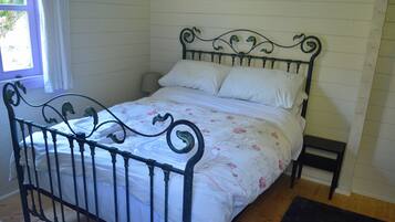 A bed with a metal frame and floral bedding in a room with wooden flooring and white walls.