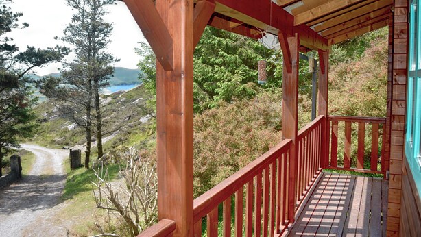 A wooden deck with a red railing overlooking a scenic landscape with trees and a distant body of water.