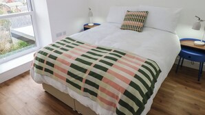 Ein Schlafzimmer mit Bett, Fenster, Nachttisch, Lampe und Blick ins Freie.