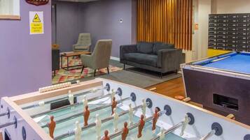 A room with a foosball table, a pool table, a sofa, and a chair.