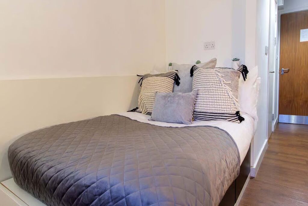 A neatly made bed with a quilted bedspread, several pillows, and a small bedside table with a lamp.