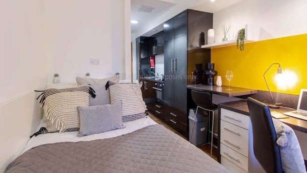 Ein modernes Schlafzimmer mit Bett, Nachttischen, einem Schreibtisch und einer Küchenzeile.