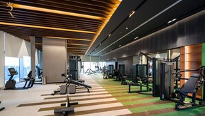 Un gimnasio moderno con varios equipos de ejercicio, suelo a rayas y un amplio muro de espejos.