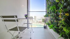 Un balcón con vistas a la ciudad y a la playa, un banco de metal y un jardín vertical.