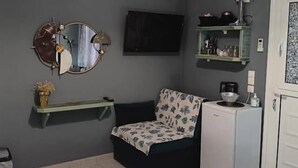 Ein gemütlicher Raum mit einem Bett, einer kleinen Couch, einem an der Wand befestigten Fernseher, einem Regal mit Küchenutensilien und einer weißen Tür.