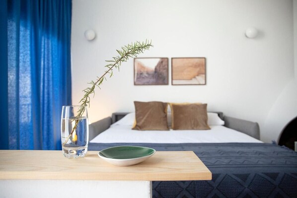 Ein Schlafzimmer mit einem Bett, Kissen, einem Nachttisch mit einem Glas Wasser und einer Pflanze, sowie zwei gerahmten Bildern an der Wand.