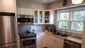 A modern kitchen with stainless steel appliances, white cabinetry, and a large window providing natural light.