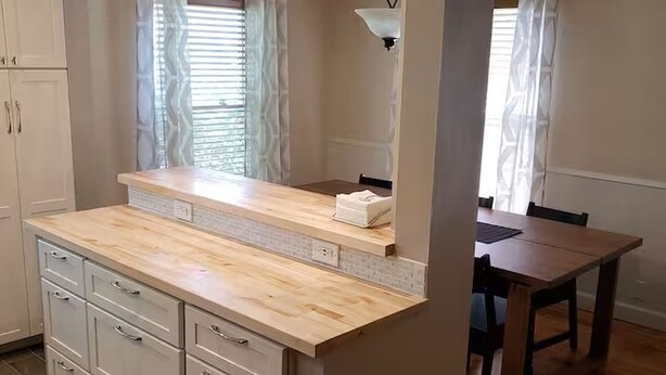 A kitchen with a wooden countertop, white cabinets, and pendant lighting.