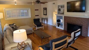 A living room with a sofa, armchairs, a coffee table, a TV, a fireplace, and a ceiling fan.