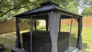 A hot tub enclosure with a roof, steps, and a wooden fence in the background.