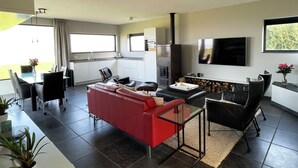 A modern living room with a red sofa, black chairs, a glass coffee table, and a TV mounted on the wall. - Modern, spacious vacation apartment with a picturesque view of Lake Tjeukesee (Oosterzee)