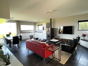 A modern living room with a red sofa, black chairs, a glass coffee table, and a TV mounted on the wall. - Modern, spacious vacation apartment with a picturesque view of Lake Tjeukesee (Oosterzee)