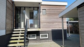 A modern building with a staircase leading to a covered entrance, a small outdoor seating area, and a brick wall. - Modern, spacious vacation apartment with a picturesque view of Lake Tjeukesee (Oosterzee)