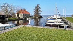 A canal with boats docked, a stone building, and a grassy area. - Modern, spacious vacation apartment with a picturesque view of Lake Tjeukesee (Oosterzee)