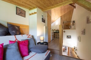 Une chambre à coucher avec un lit, des oreillers, une lampe de chevet, un plafond en bois et un couloir menant à une salle à manger.