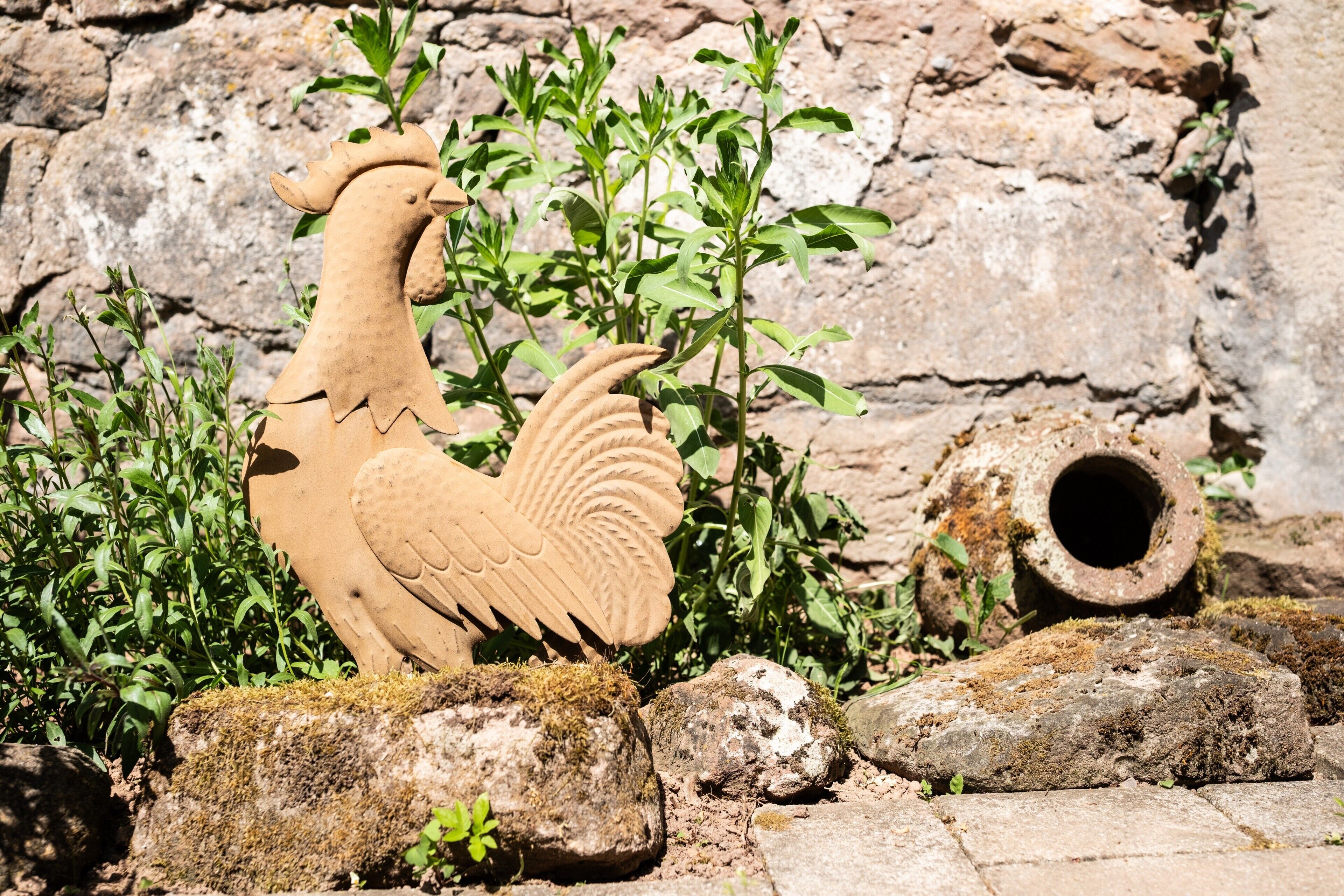 Une sculpture de coq, une pipe en pierre et de la verdure, le tout dans un décor extérieur rustique.