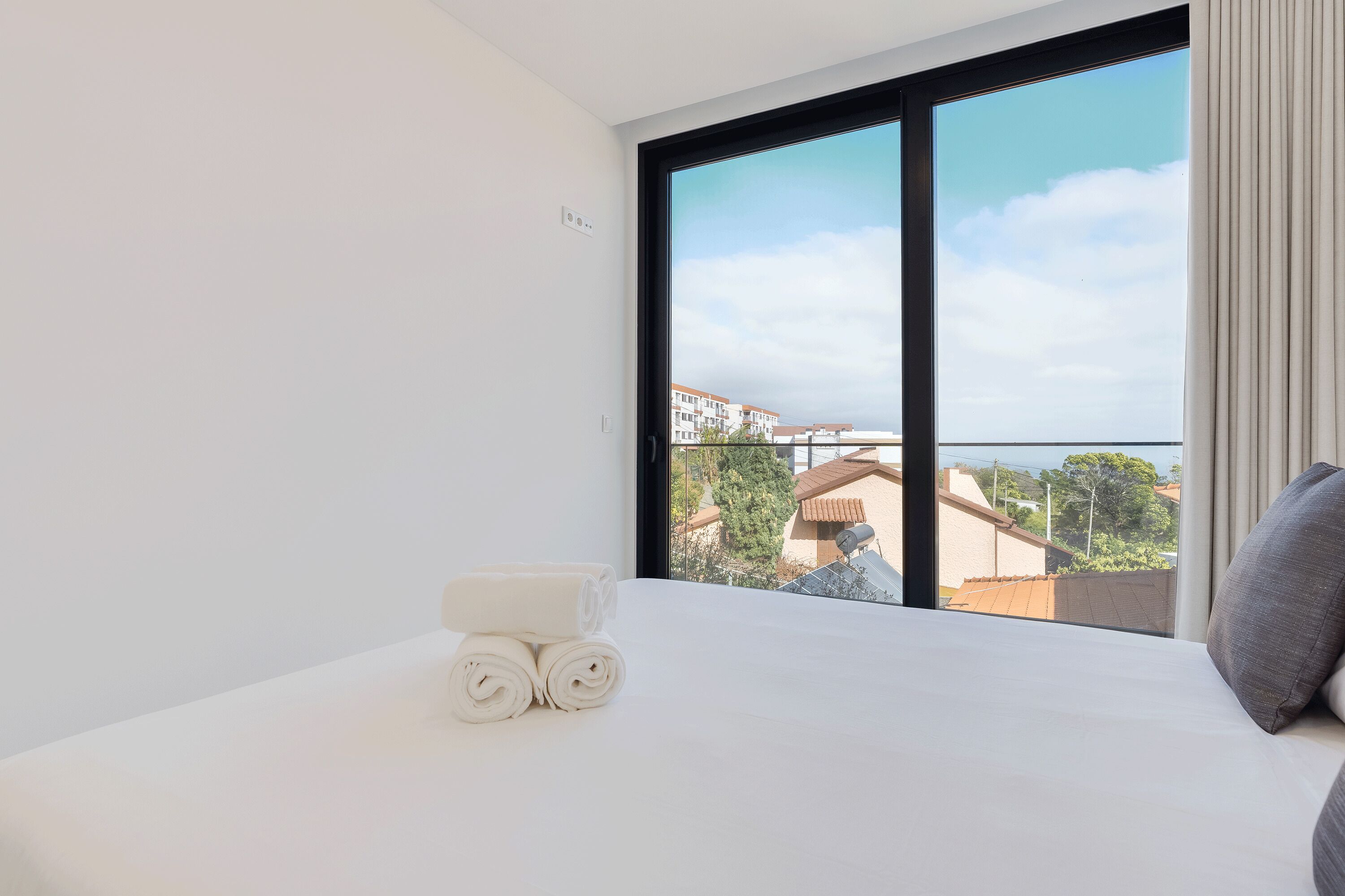A hotel room with a large window, a neatly made bed, and a view of buildings and trees.