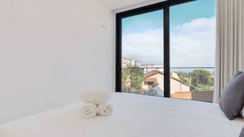 A hotel room with a large window, a neatly made bed, and a view of buildings and trees.