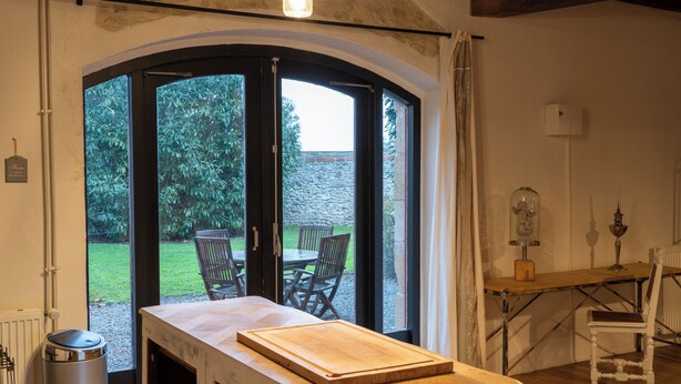 Eine Küche mit Holzauskładung, einem Tisch und Stühlen. Ein Fenster bietet Blick auf einen Garten und eine Steinmauer.